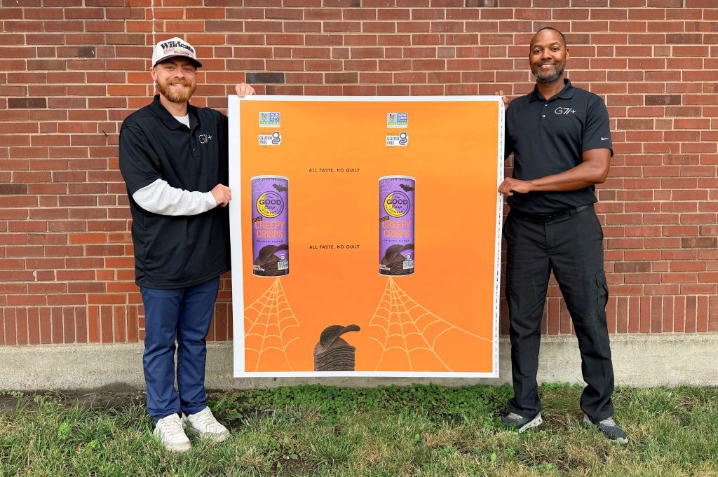 Two Litho Press team members holding a large-format printed Halloween top sheet
